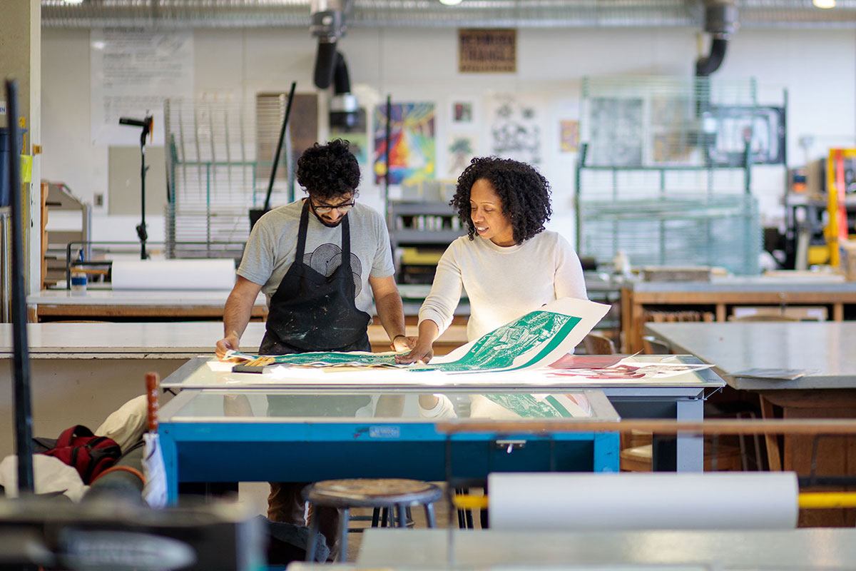 An art professor demonstrates printmaking technique to a student.